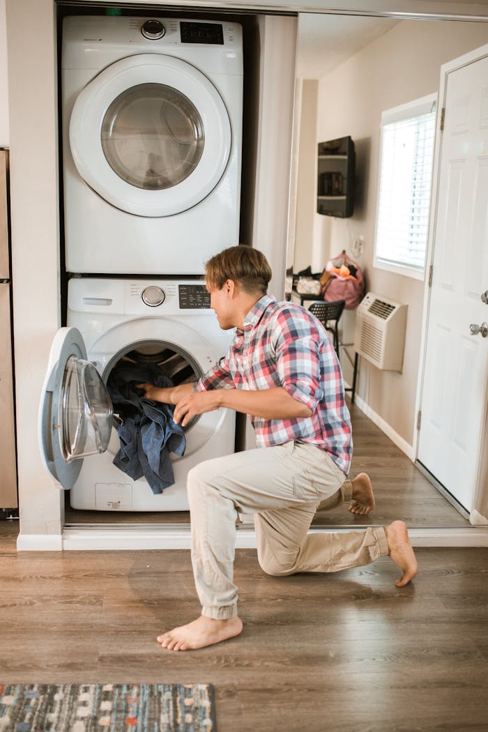 mobile-02 A man loading clothes into a front-loading washing machine in a modern, well-lit laundry room.