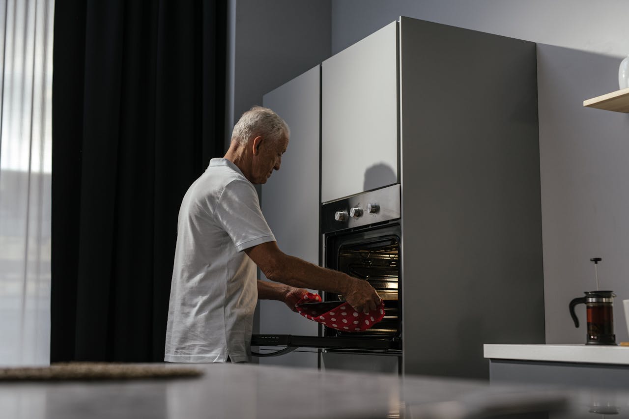 creative Elderly man using oven in a modern kitchen interior with a focus on light and shadows.
